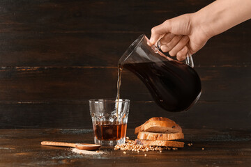 Woman pouring tasty kvass from jug into glass on wooden background