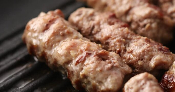 Grilling meat on a grill pan. Smoking sausages are turned over with tongs. Food preparation. Chevapi Traditional Balkan grilled sausages. Close up. High quality footage