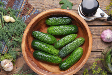 Bowl with fresh cucumbers and ingredients for canning on wooden background