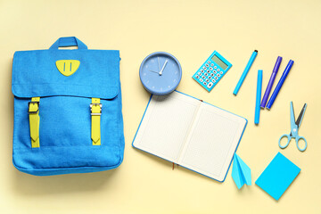 School backpack with alarm clock different stationery on pale yellow background