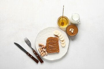 Plate of toast with peanut butter, banana and nuts on white background
