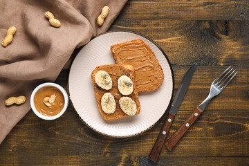 Plate of toasts with peanut butter, banana and poppy seeds on wooden background