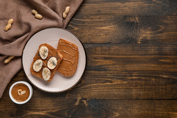 Plate of toasts with peanut butter, banana and poppy seeds on wooden background