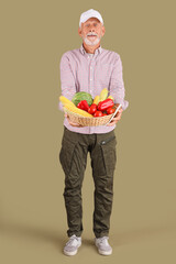 Mature male farmer with wicker basket full of different ripe vegetables on green background