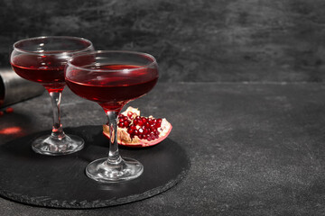 Board with glasses of Cosmopolitan cocktail and pomegranate on black background