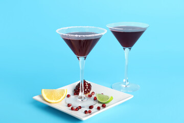 Glasses of Cosmopolitan cocktail with pomegranate and lemon on blue background