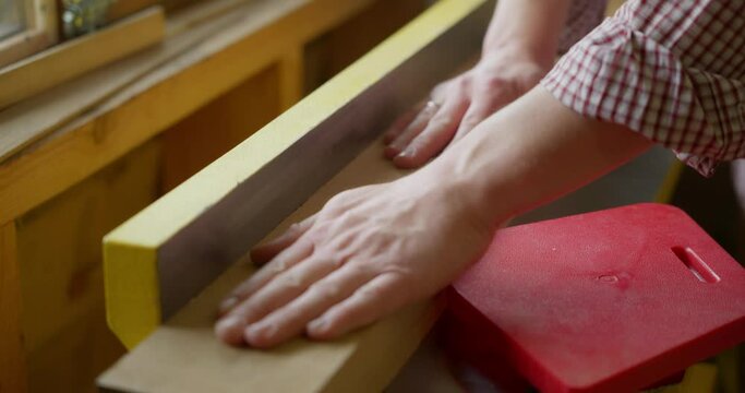 Close-up of the hands of a male carpenter or woodworker working an oak plank on a jointer planer in a carpentry or woodwork workshop. Processing of the tree. High quality 4k footage