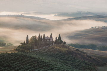 Atmospheric sunrise mist through the valley of Val d'Orcia and a rustic farmhouse in the scenic...