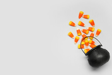 Halloween composition with overturned cauldron and candy corns on grey background