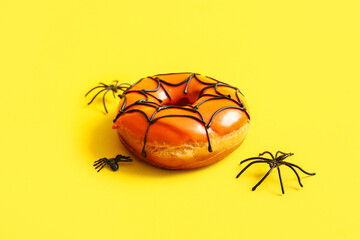 Tasty donut for Halloween with spiders on yellow background