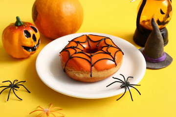 Plate of tasty donut with decorations for Halloween on yellow background