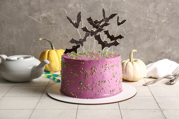 Tasty cake decorated for Halloween on table near grey wall