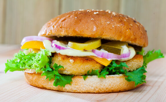 Image of burger with chicken cutlet, cucumber, lettuce and onion at plate