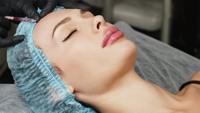 Woman getting beauty injection in cosmetic clinic. Close up cosmetologist doing botox injection in forehead to patient in beauty clinic. Rejuvenation, injectable cosmetology concept