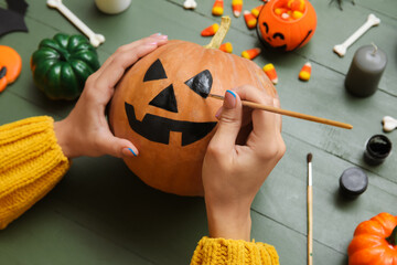 Woman painting Halloween pumpkin at green wooden table