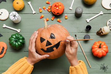 Woman painting Halloween pumpkin at green wooden table