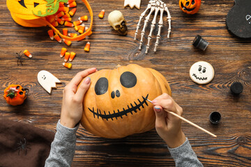 Woman painting Halloween pumpkin at wooden table