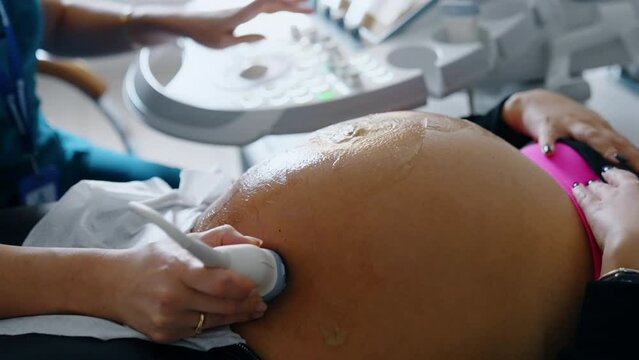 Big belly of a pregnant woman with gel on it. Hand of doctor moves ultrasound device by the patient's abdomen. Close up.
