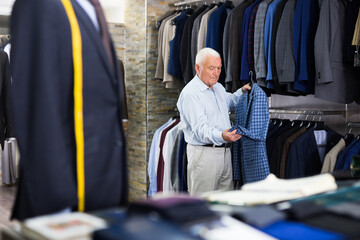 Happy mature man holding classic jacket in clothing store