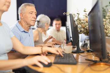 Concentrated elderly man immersed in using computer in library. Concept of integration of older...
