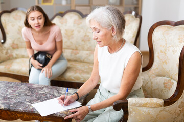 Woman realtor helping an elderly woman to sign an apartment lease agreement
