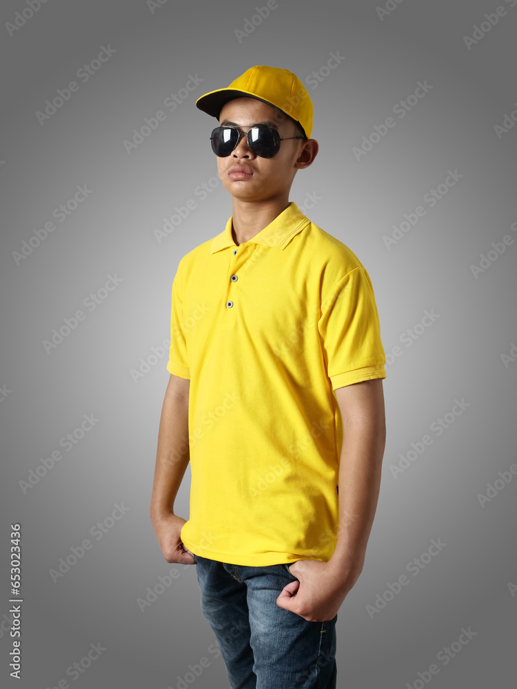 Canvas Prints Young Asian teenage boy wearing yellow collared shirt, hat and sunglasses standing with hands on hip over grey background, t-shirt template