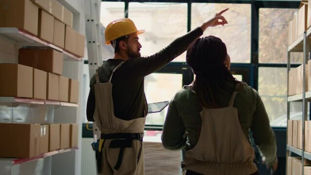 African american manager and trainee preparing warehouse orders for delivery, using tablet to verify shipping informations, crosschecking online data and scanning stock labels in distribution center