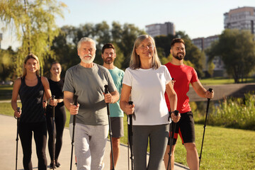 Group of happy people practicing Nordic walking with poles in park
