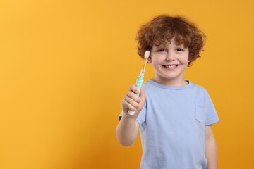 Cute little boy holding electric toothbrush on yellow background. Space for text