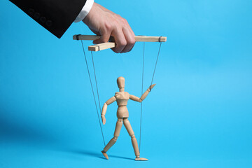 Man pulling strings of puppet on light blue background, closeup