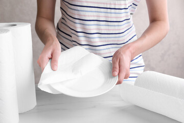 Woman wiping plate with tissue paper at white marble table, closeup