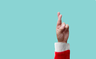 hand of a person dressed as santa claus crossed fingers on blue background - luck concept