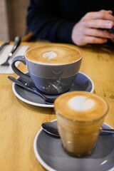 A grey coffee cup and saucer of flat white coffee, and a smaller piccolo in a glass (both with...