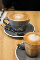 A grey coffee cup and saucer of flat white coffee, and a smaller piccolo in a glass (both with...