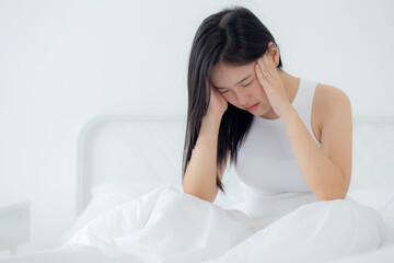 Fototapeta premium Young asian woman sitting on bed pain headache in the bedroom at home, unhappy female exhaustion and sick headache, anxiety and unwell, dizziness and disorder, medical and health concept.