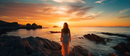Woman observing ocean sunset from the rocky shore in a dramatic silhouette like manner embracing the concept of being an outsider