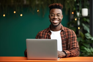 Smiling young black male college student sitting on his desk using his laptop looking at the camera