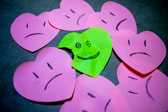 Concepto de actitud positiva elaborado con papeles en forma de coraz&oacute;n, donde todos est&aacute;n tristes y uno sonr&iacute;e a pesar de estar arrugado y roto.