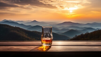 A whiskey glass and a bottle on a bar table In the background are mountains and a sea of mist at sunset. - obrazy, fototapety, plakaty
