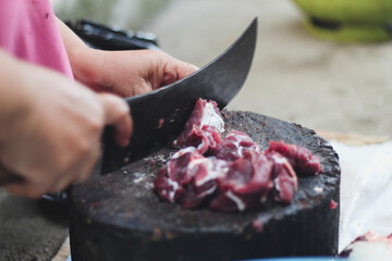 Cutting fresh red meat with a sharp, hand-held knife and tusks on a large piece of wood