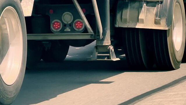 Tires and wheels of a passing semi-truck trailer on interstate highway pavement, in closeup hand held clip.