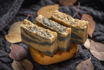 Pieces of handmade natural soap on a wooden soap dish against the background of a warm sweater and dry leaves. Concept of a cozy autumn atmosphere, organic cosmetics for the skin care