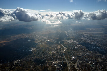 Aerial view from airplane window at high altitude of distant city covered with white puffy cumulus...