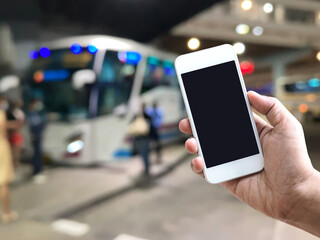 hand holding mobile phone over blur background of bus platform at night. - 653064266