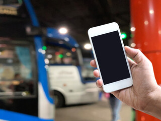 hand holding mobile phone over blur background of bus platform at night. - 653064283