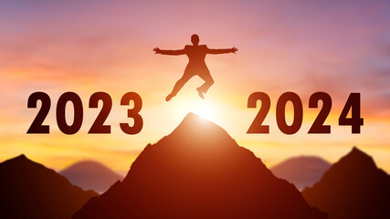 Silhouette of a person leaping from 2023 to 2024 on the top of the mountain background. Happy New...