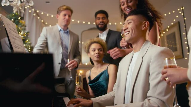 Group of friends singing and playing at piano celebrating at Christmas or new year party together - shot in slow motion