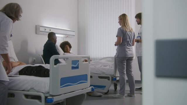Nurse and male doctor with digital tablet computer explains medical tests results to African American family. Mature female medic checks broken leg in bondage of teen patient in hospital room.