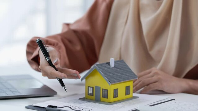 House broker representing an Asian Muslim woman presents model home plans and explains business contracts, rentals, purchases, mortgages, loans or home insurance in the office.