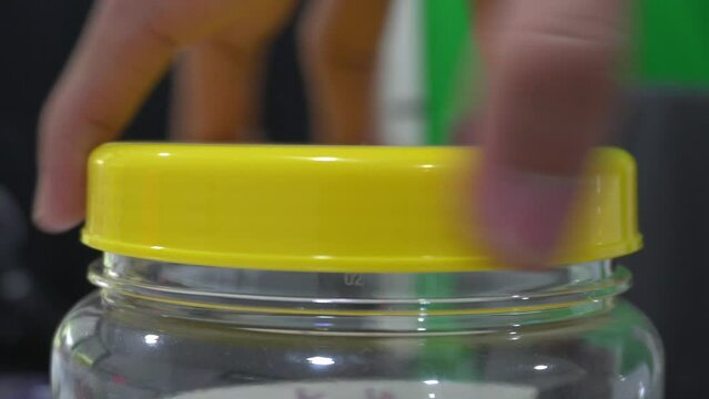 Male hand turn open yellow cap from plastic box, put object inside and close the cap. Home living and tool concept